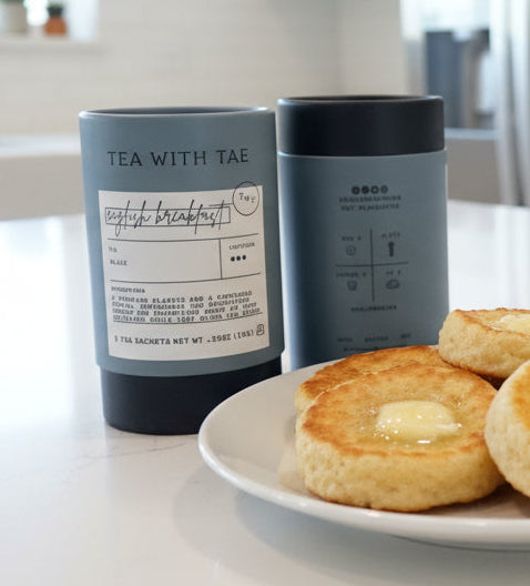 Biscuits with butter on a plate with a bowl of jam, two tumblers labeled 'Tea with Tim' in the background.