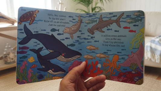 Colorful children's book with underwater illustrations held by a hand in a living room.