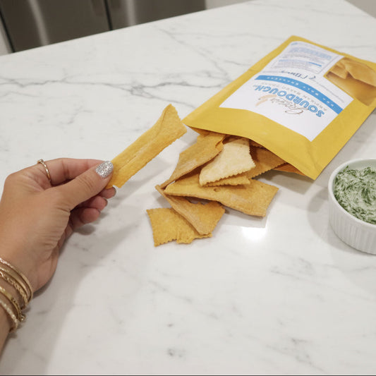 Hand holding a bag of tortilla chips with a visible brand label on a dark surface.