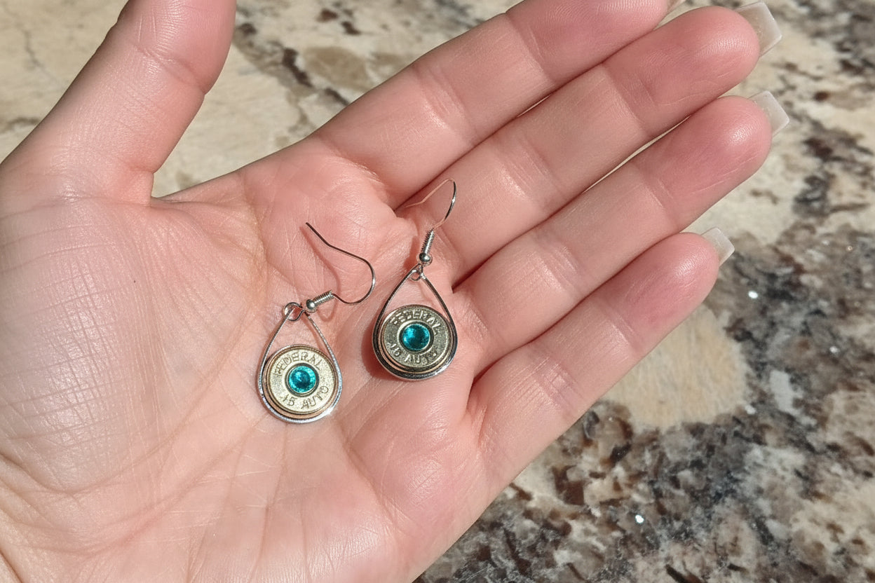 Hand holding two small earrings with a stone surface background