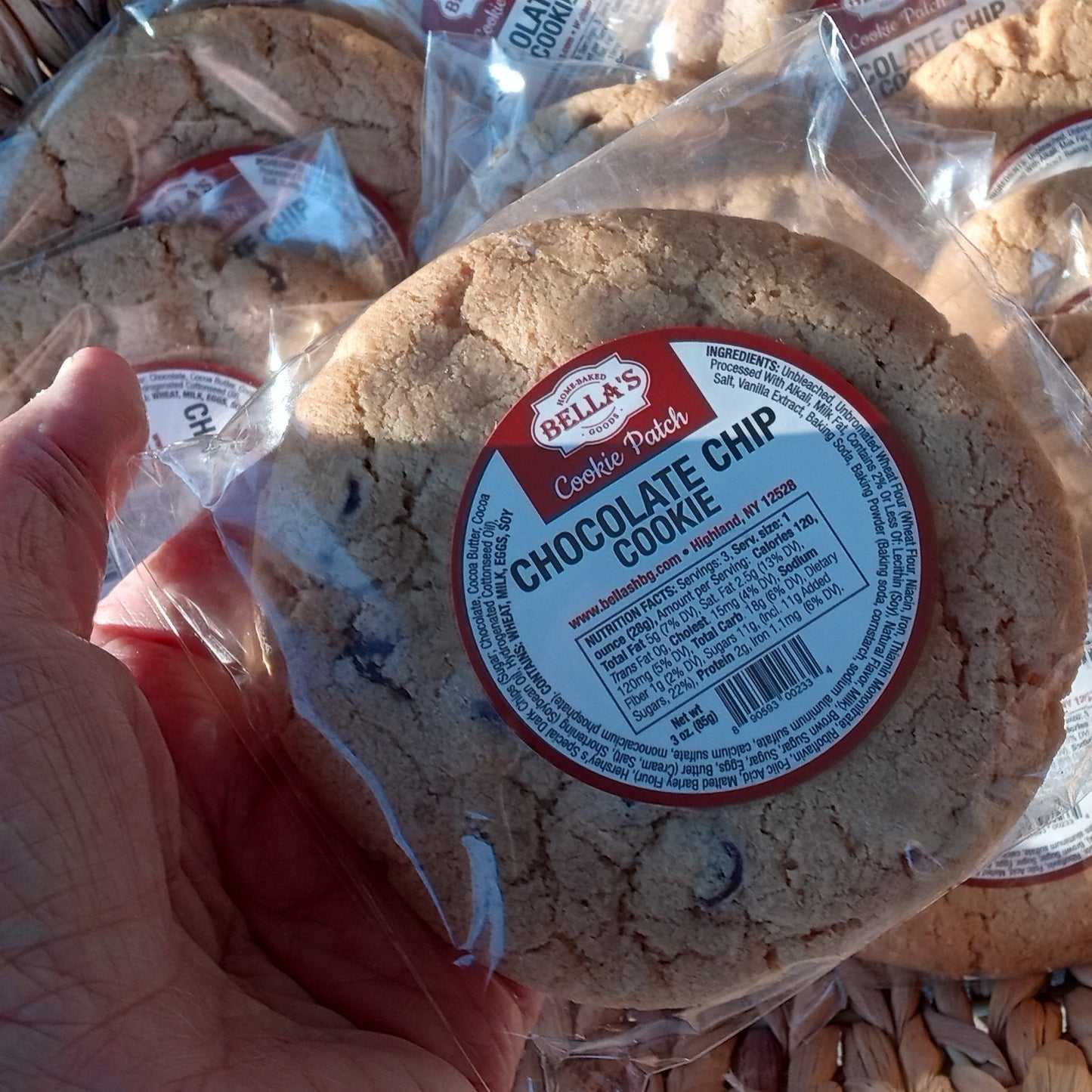 Hand holding a package of chocolate chip cookie, with more packages in the background.