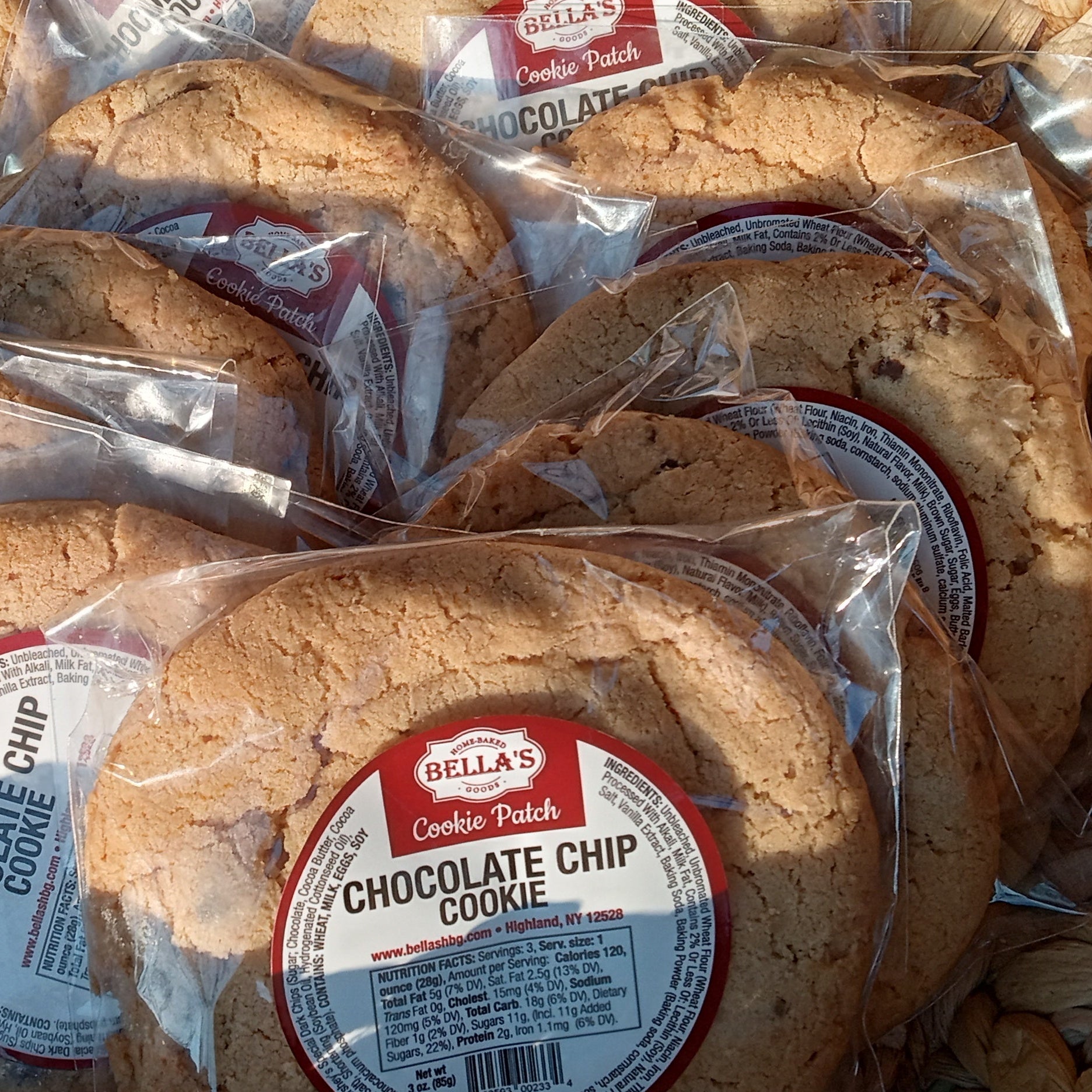 Baked goods, specifically chocolate chip cookies, in clear plastic packaging on a woven surface.