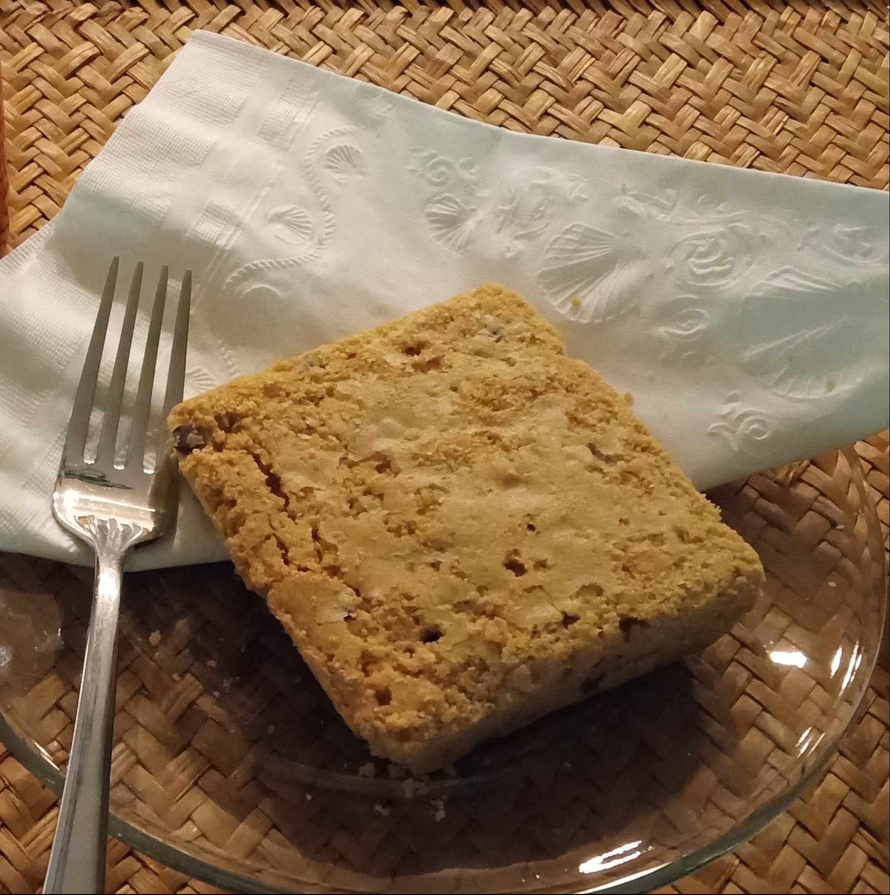 Square piece of bread on a glass plate with a fork and an orange mug of coffee on a woven mat.