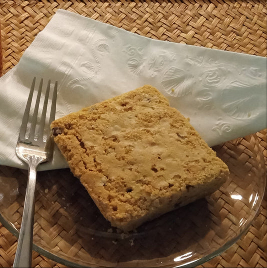 Square piece of bread on a glass plate with a fork and an orange mug of coffee on a woven mat.