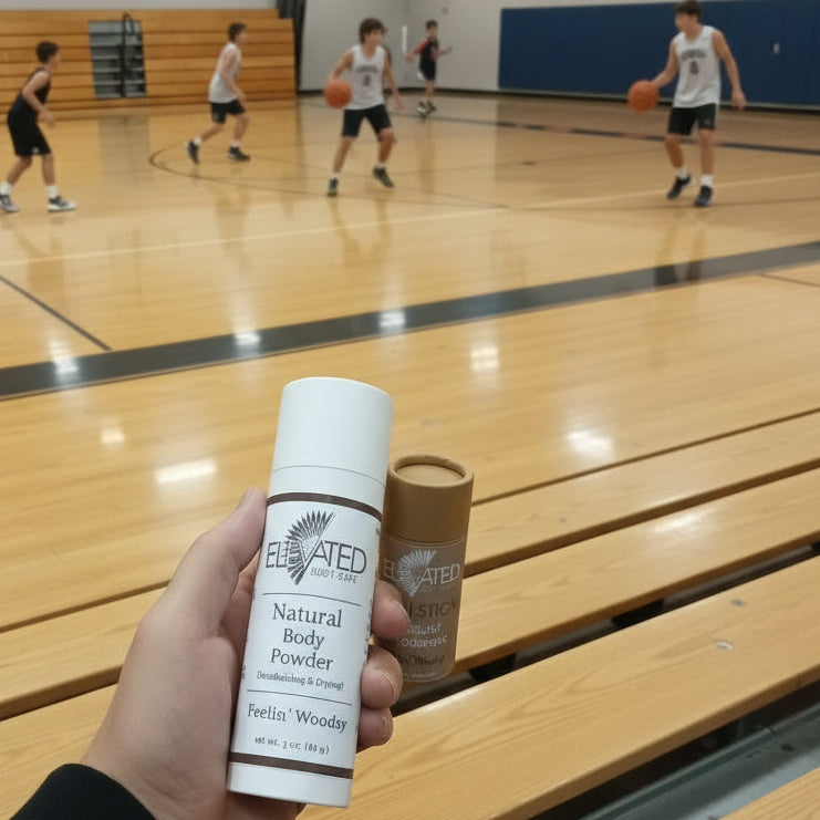 Hand holding a bottle of 'Elated' natural body powder on a wooden surface.