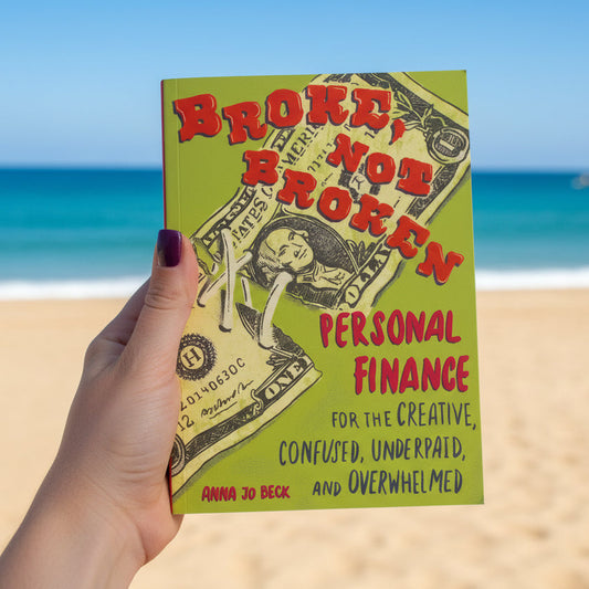 Book titled 'Broken, Not Broken: Personal Finance for the Creative, Confused, Underpaid, and Overwhelmed' held by a hand