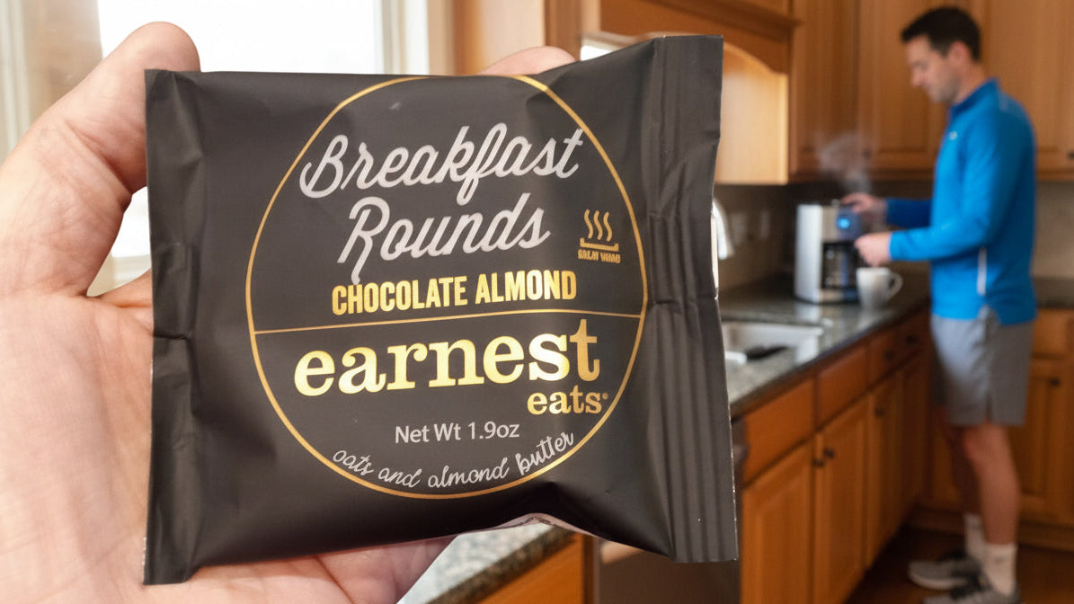 Hand holding a 'Earnest Eats' chocolate almond breakfast rounds package in a kitchen setting.