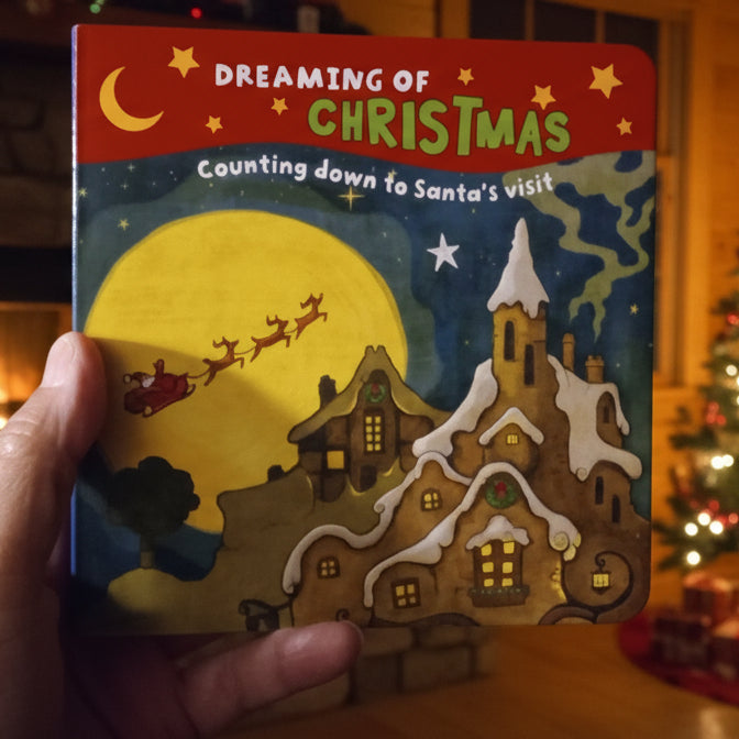 Children's book titled 'Dreaming of Christmas' held by a hand on a wooden floor.