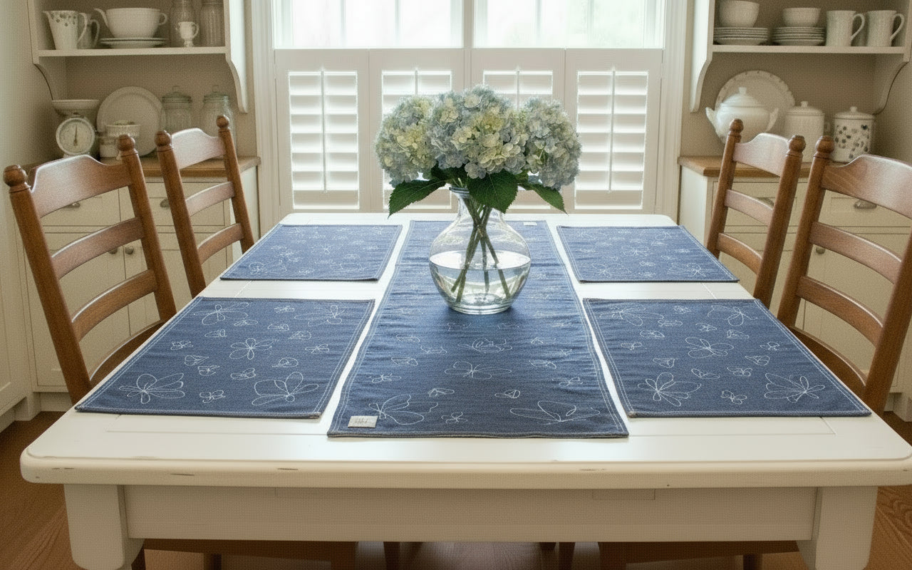 Set of blue placemats on a wooden table with a vase and flowers in the center.