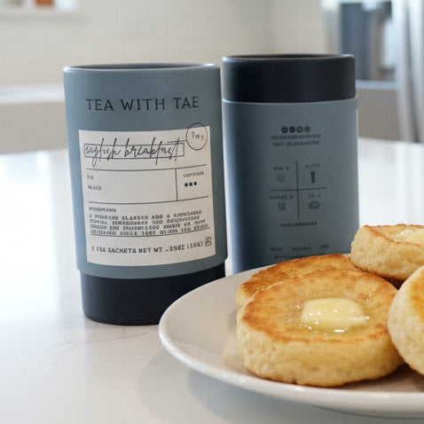 Biscuits with butter on a plate with a bowl of jam, two tumblers labeled 'Tea with Tim' in the background.