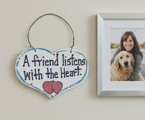 Heart-shaped sign with 'A friend listens with the heart' text held by a hand against a white background.