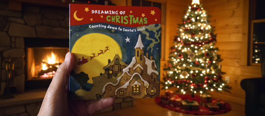 Children's book titled 'Dreaming of Christmas' held by a hand on a wooden floor.