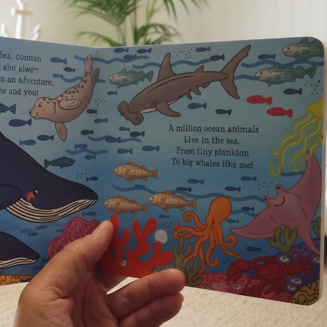 Colorful children's book with underwater illustrations held by a hand in a living room.