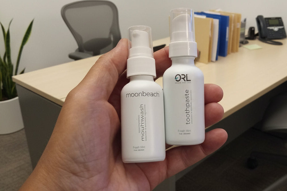 Two ORL skincare bottles held in a hand with a patterned rug and brown surface in the background.