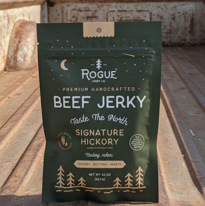 Package of Rogue Jerky Co. beef jerky on a rustic wooden surface with a truck in the background.
