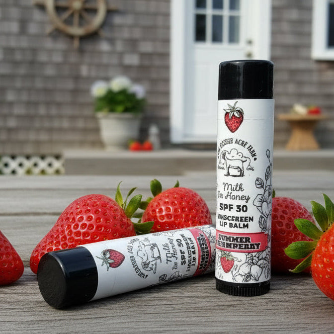 Two lip balm tubes with strawberry design on a wooden surface with strawberries.