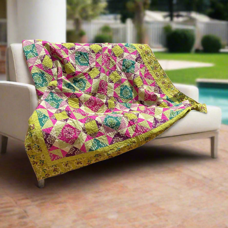 Colorful quilt draped over a white chair outdoors with a pool and garden in the background