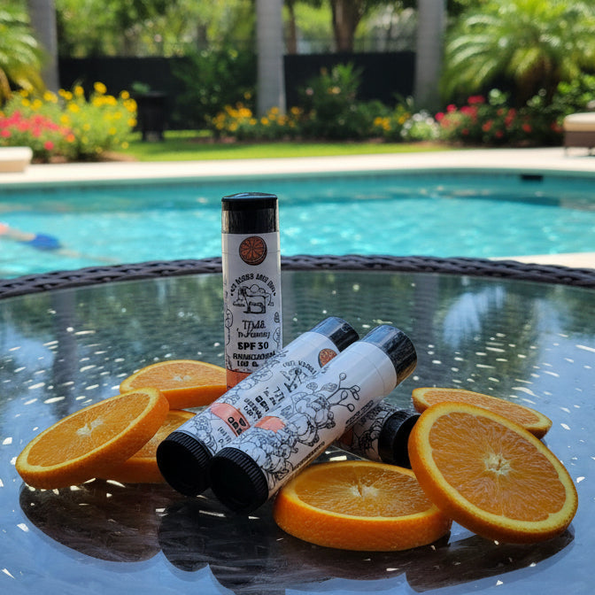 Two bottles and orange slices on a glass table by a pool with a person swimming in the background.