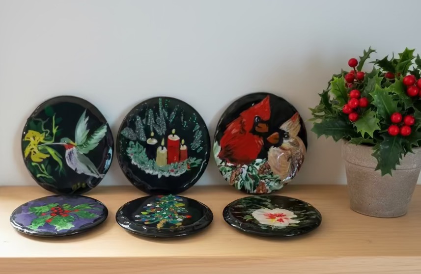 Set of decorative plates with various designs on a wooden shelf, accompanied by a potted plant with red berries.