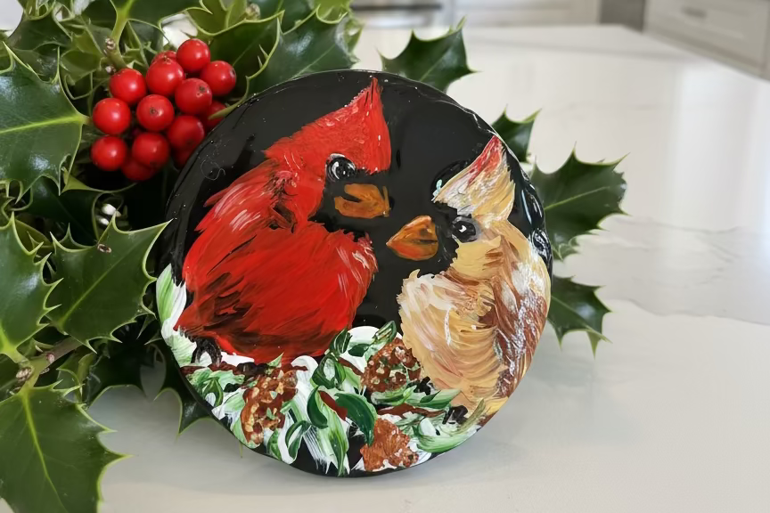 Round ceramic tile with a painted red cardinal and green leaves on a white background