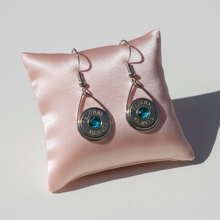 Pair of earrings with turquoise stones on a white cloth with a blue box in the background.