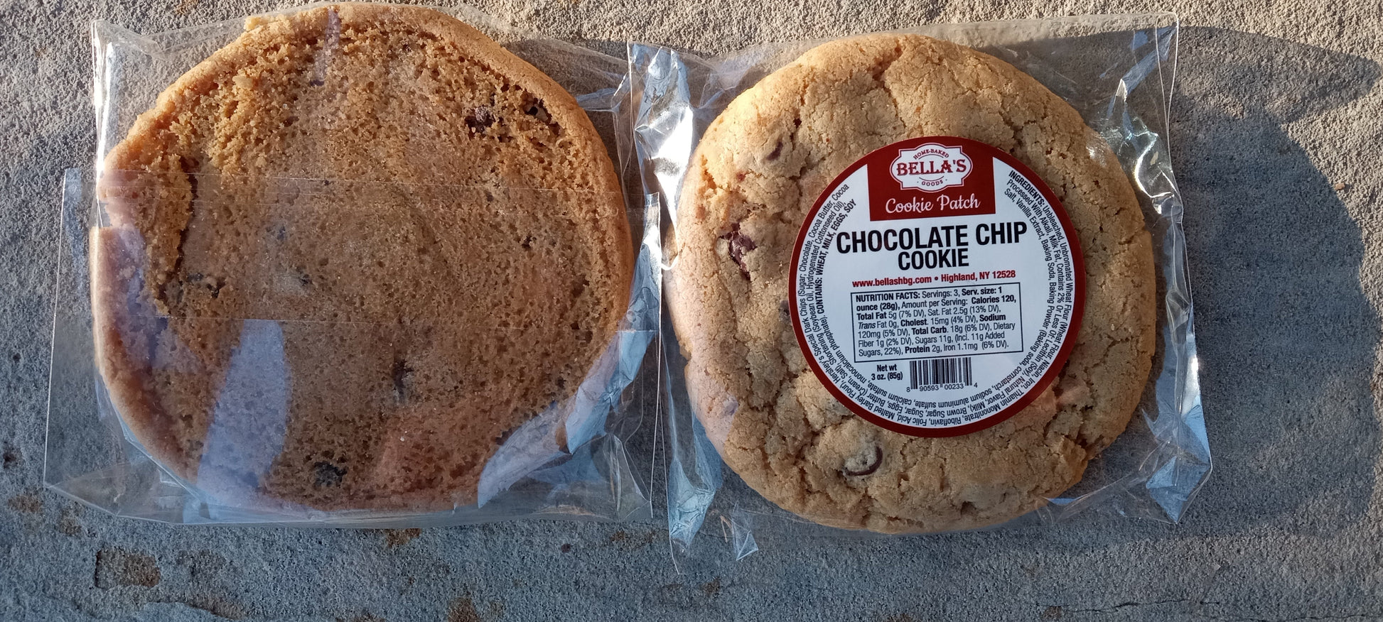Two chocolate chip cookies in clear packaging on a concrete surface