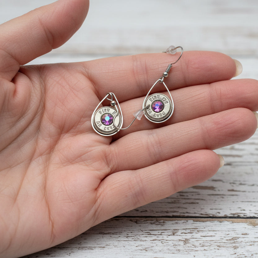 Silver earrings with gemstones held in a hand against a stone background