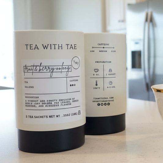 Two packages of 'Tea with Tae' tea and a teacup on a kitchen counter.