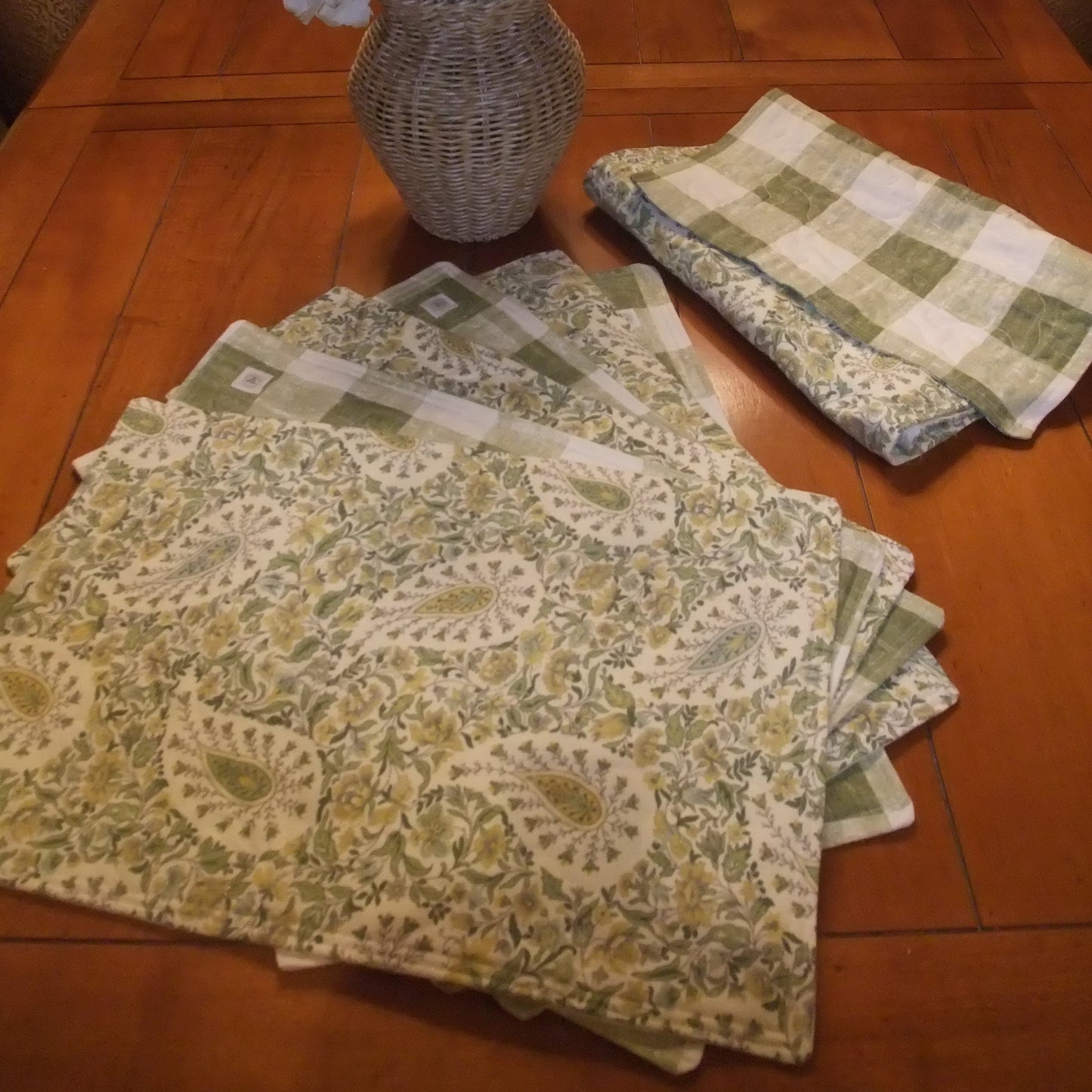 Patterned green napkins on a wooden table with a vase of flowers.