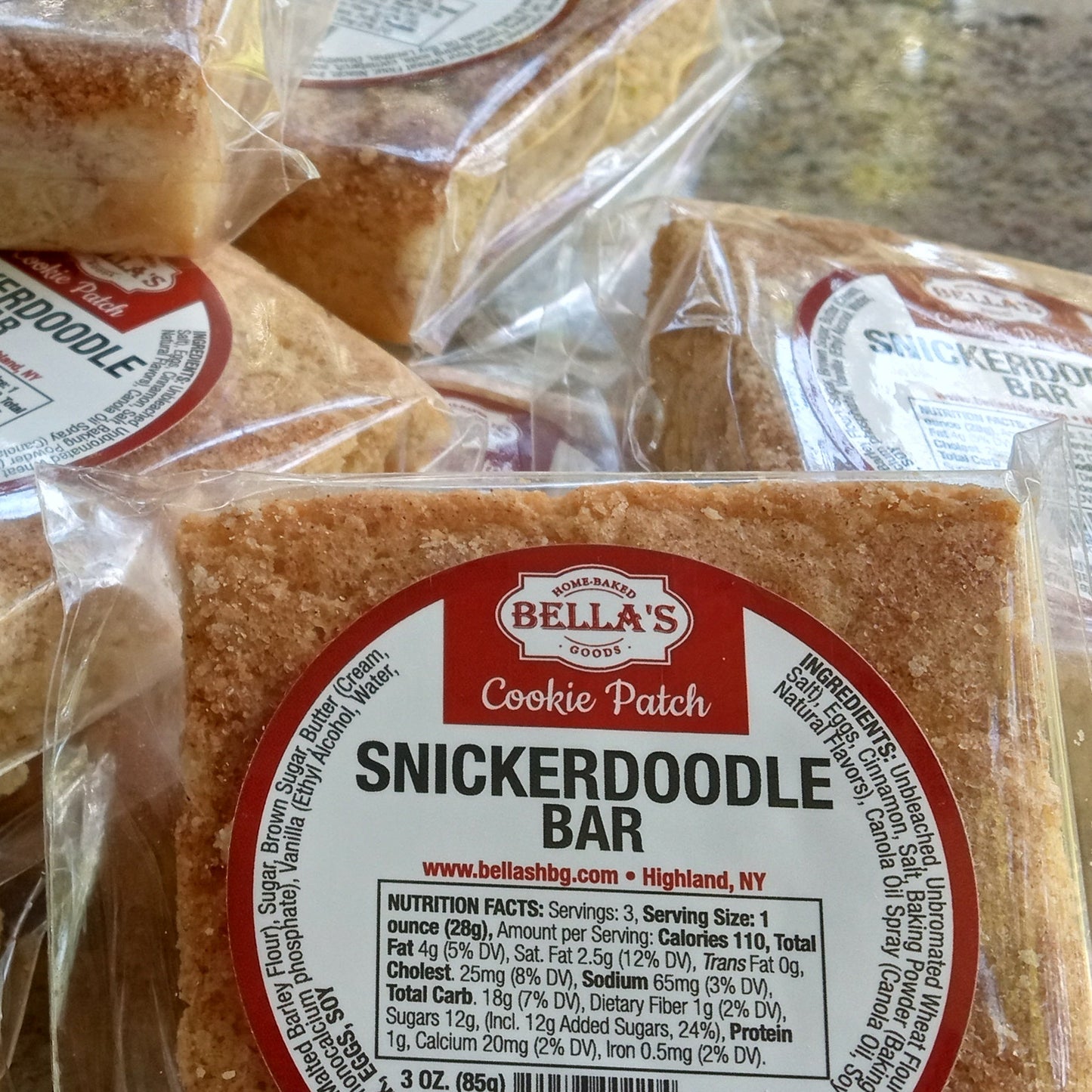 Bella's Snickerdoodle Bars in clear packaging with red labels on a marble surface.