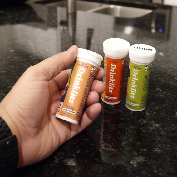 Hand holding four 'DrinkLite' energy drink tubes on a dark surface